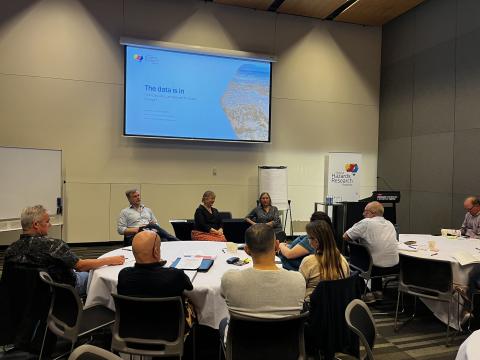 A group of workshop particiapants sitting around tables with 3 researchers talking to the group