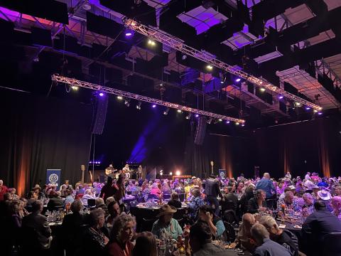 People sitting at gala dinner tables in front of stage and purple liights