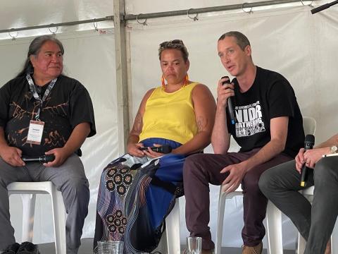 Three people sitting down, man on right speaking into microhpone