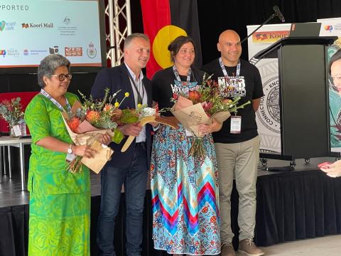 Four people holding flowers smiling at camera in front of stage